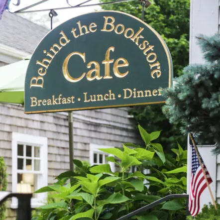 Sign of Behind the Bookstore Cafe surrounded by flowers and plants