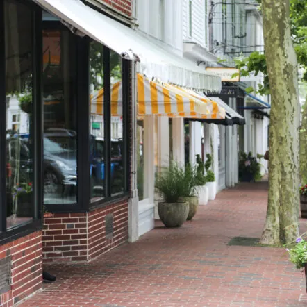 Brick sidewalk lined with shops and yellow striped awnings in Edgartown Downtown