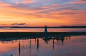 Lighthouse and dock at sunset with colorful sky reflections on the water