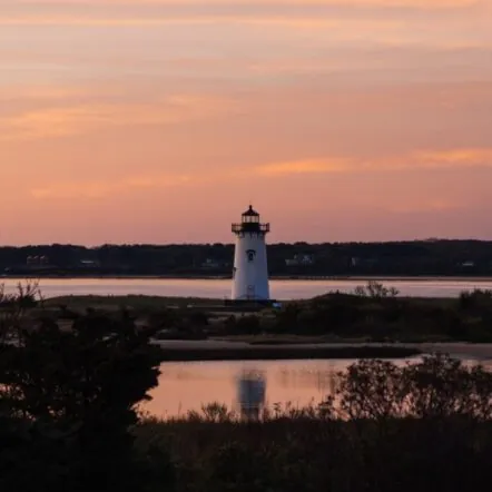 Edgartown Lighthouse at sunset with water and trees in the foreground
