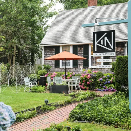 Kin Arts and Clothing exterior view and garden with flowers, patio seating, and Kin sign