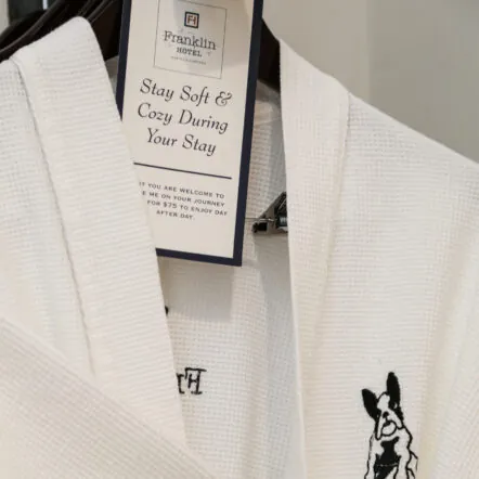 White Franklin Hotel robe with bulldog logo hanging on a hook
