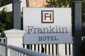 Franklin Hotel sign with white fance and greenery in the background